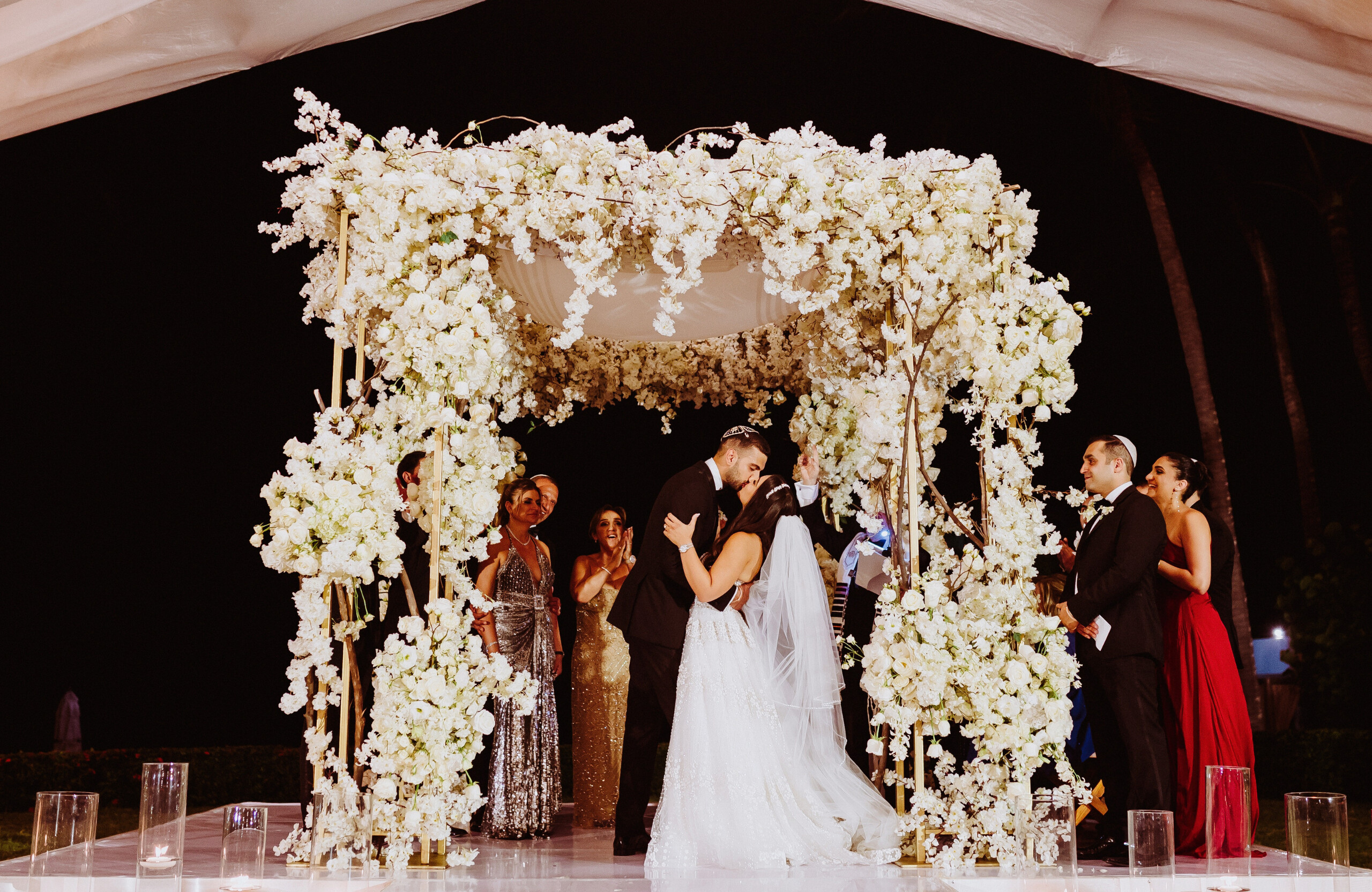 bride and groom kissing under white floral Chuppah